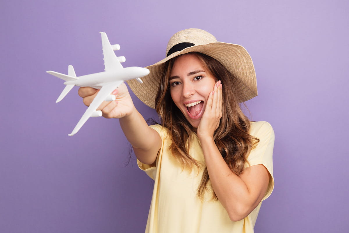 Young beautiful woman beige t-shirt summer hat holding toy looking camera happy, excited airplane standing purple background